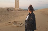 Schwangere Person steht auf einer Sanddüne
